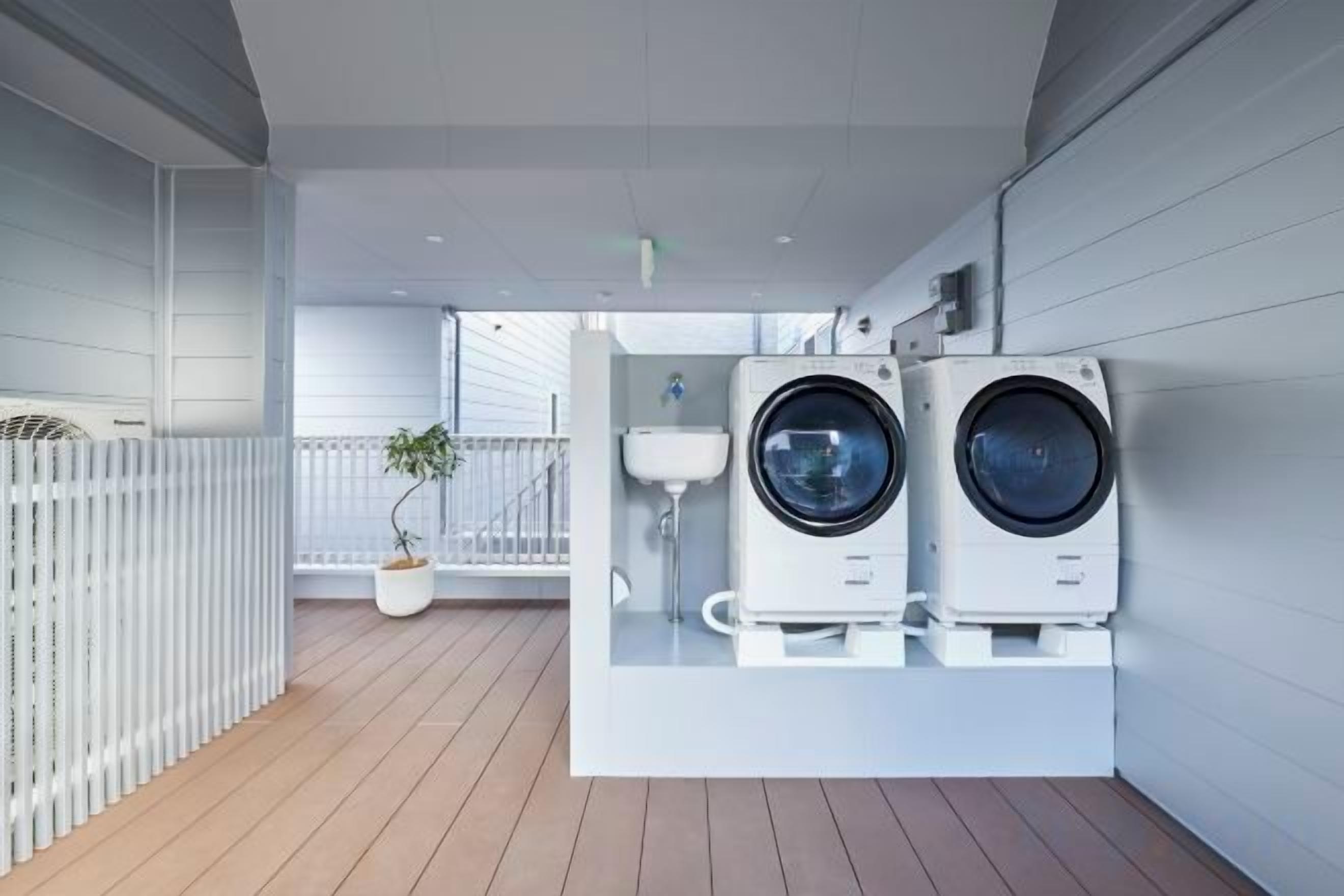 Un espace buanderie compact comprenant deux machines à laver et un évier, le tout délimité par un mur blanc et un plancher en bois.