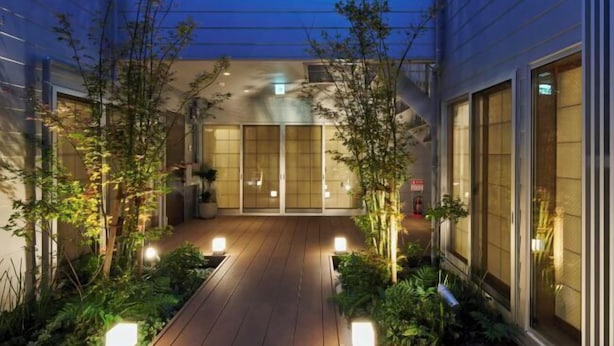 A courtyard with wooden flooring, potted plants, and a building with large windows and a sliding door. - Reikyo Garden Osaka (Osaka)