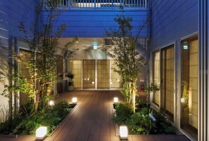 A courtyard with wooden flooring, potted plants, and a building with large windows and a sliding door. - Reikyo Garden Osaka (Osaka)