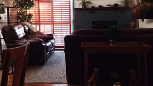 A cozy living room with a fireplace, a leather sofa, a dining table, and a large window with blinds. - Overlooking Amazing Pool, 2 King ensuite Condo, location, location, location! (Sedona)