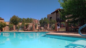 A clear blue pool with a diving board, surrounded by lounge chairs and a fenced area with a building in the background. - Overlooking Amazing Pool, 2 King ensuite Condo, location, location, location! (Sedona)