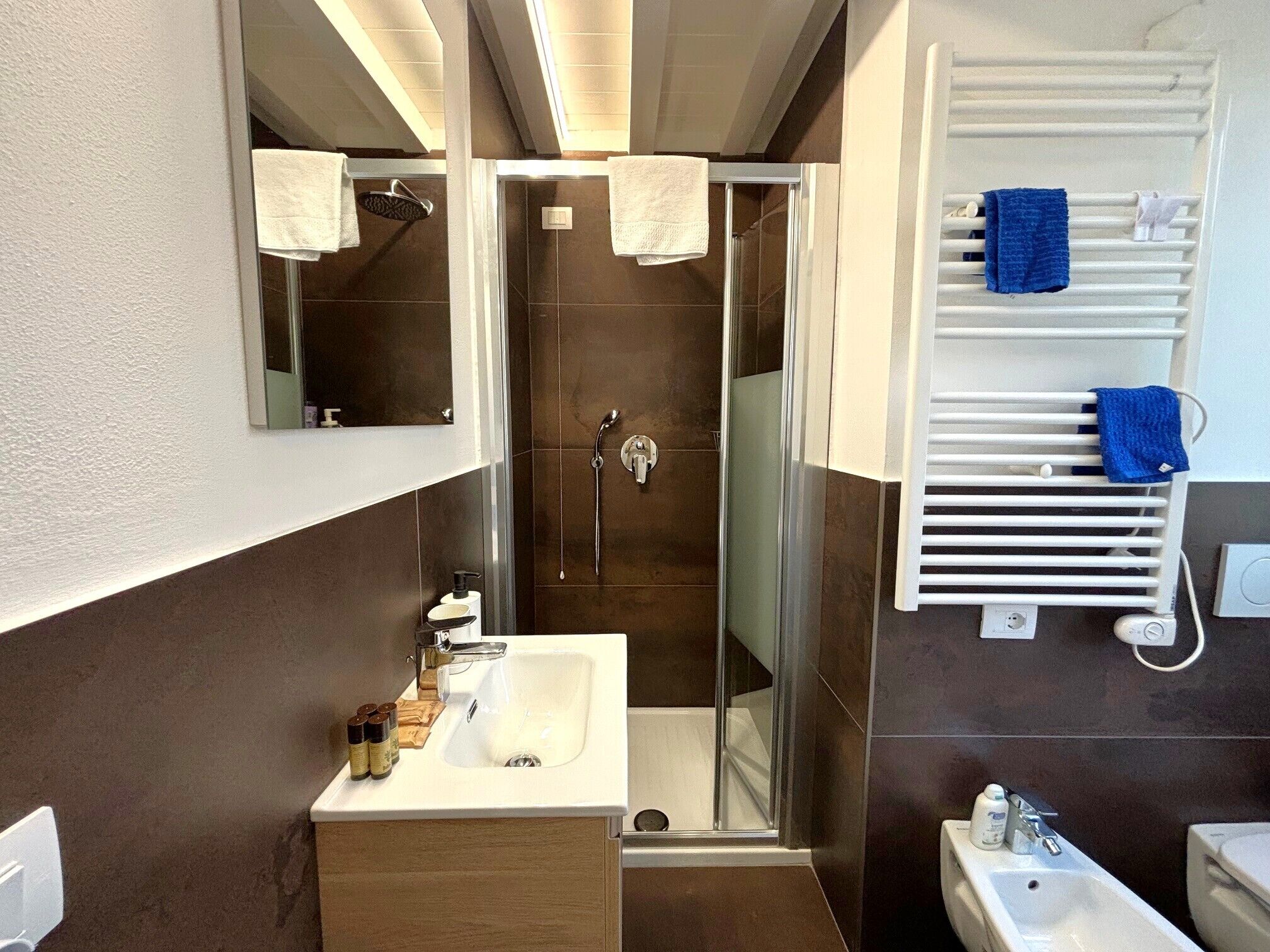 A modern bathroom with a glass-enclosed shower, a white sink, and a towel rack with multiple towels.
