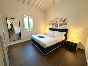 A bedroom with a bed, bedside tables, a mirror, and artwork on the wall. - Purple Lily Apartment (Firenze)