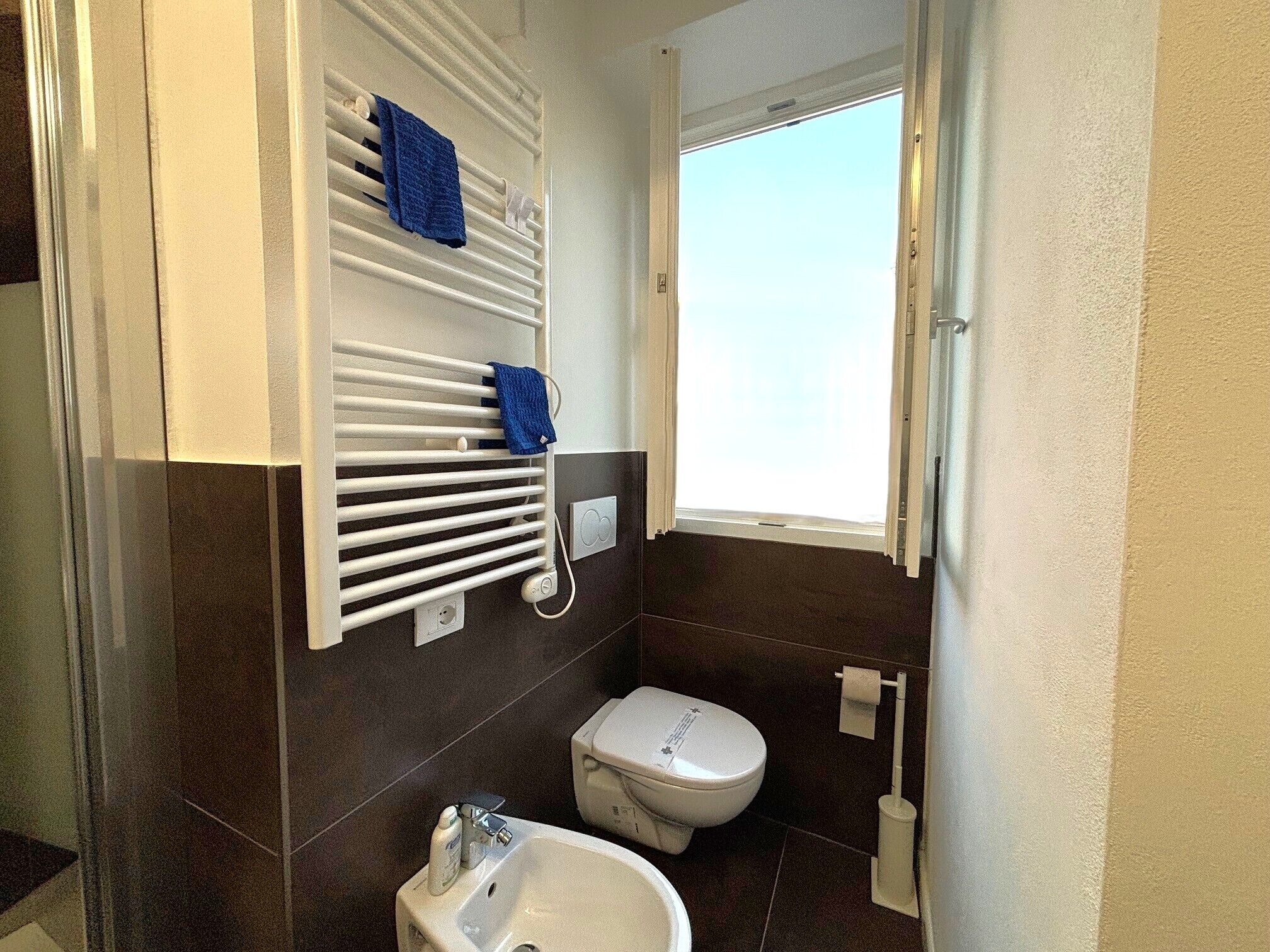 Une salle de bain avec un radiateur blanc, des toilettes, un lavabo et une fenêtre.
