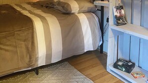 A cozy bedroom with a bed, a shelf with books, and a lamp. - LA P'TITE MAISON DU CANAL (Drevant)