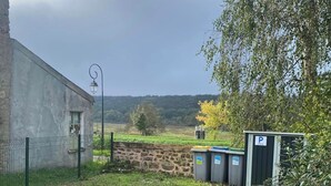 A rural setting with a building, a fence, and a parking area with bins. - LA P'TITE MAISON DU CANAL (Drevant)