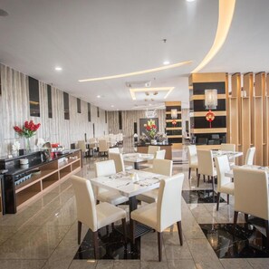 A modern restaurant with white tables and chairs, a central bar area, and decorative elements like flowers and a red ornament. - Lintas Platinum Hotel (Kota Kinabalu)