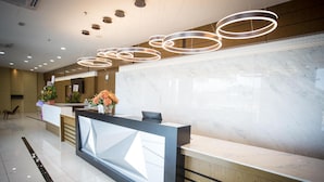 A modern reception desk with a marble counter, wooden paneling, and a series of circular pendant lights. - Lintas Platinum Hotel (Kota Kinabalu)
