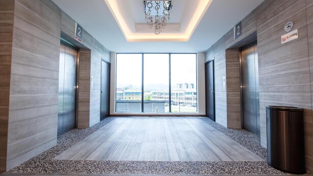 A modern elevator lobby with a city view, two elevators, and a no-smoking sign. - Lintas Platinum Hotel (Kota Kinabalu)