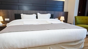 A large bed with a headboard, two bedside lamps, and a green chair. - Lintas Platinum Hotel (Kota Kinabalu)