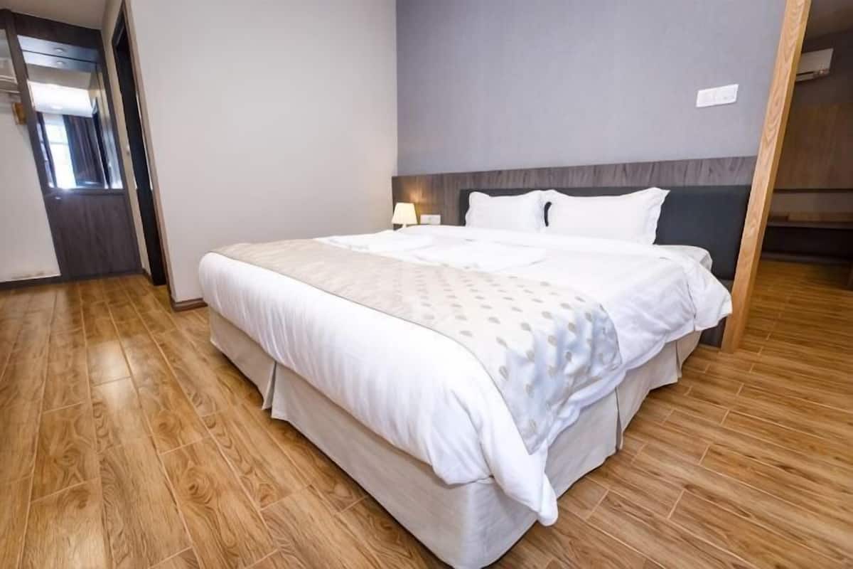 A hotel room with a large bed, wooden flooring, a headboard, and a nightstand with a lamp.
