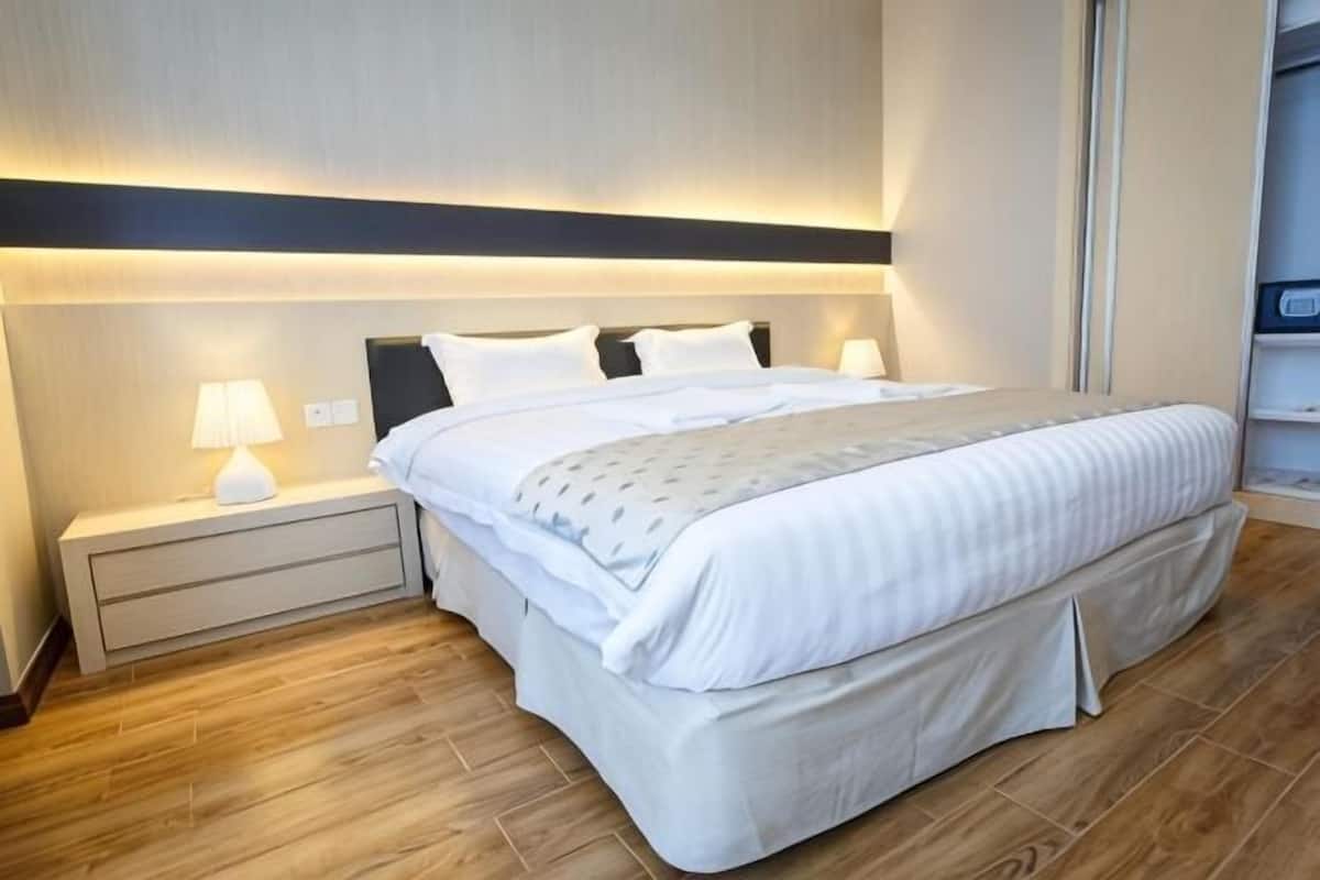 A neatly made bed with a headboard, bedside tables with lamps, and a wooden floor.