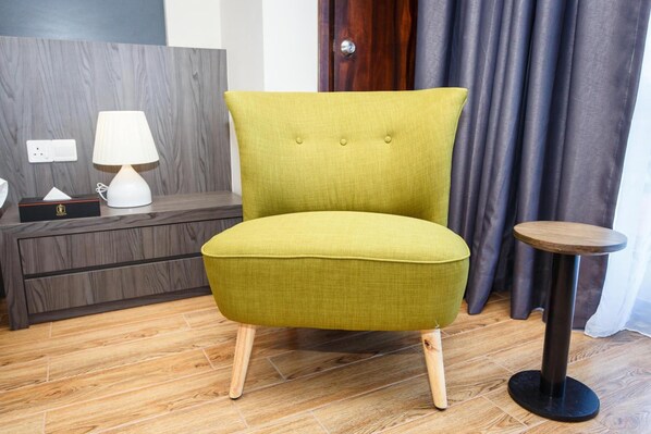 Un fauteuil vert recouvert de tissu, avec des pieds en bois, une petite table ronde, une lampe et une boîte à mouchoirs, le tout posé sur un plancher en bois.