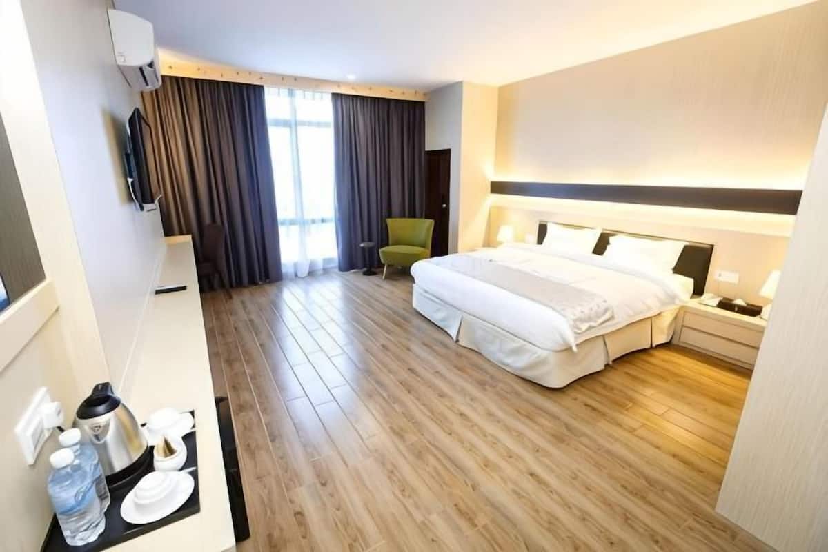 A hotel room with a bed, bedside table, lamp, chair, and a desk with a kettle and glasses.
