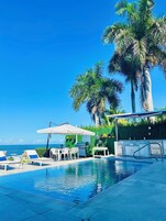 Un área de piscina con sillones de descanso y sombrillas, una parrilla y vistas al océano.