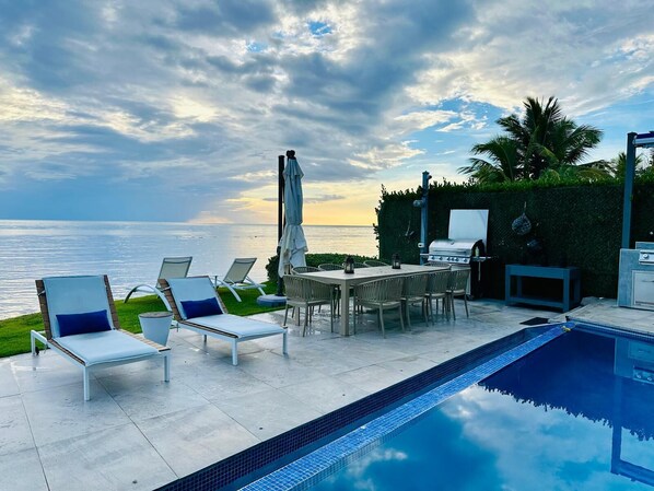 A poolside area with lounge chairs, a dining table, and a grill. - VILLA JOYUDA (Cabo Rojo)