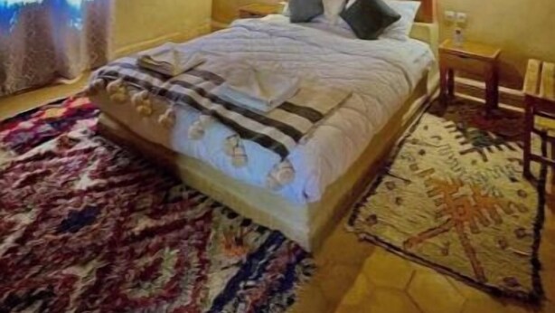 A bedroom with a wooden ceiling, a bed with pillows, a nightstand, and a patterned rug.