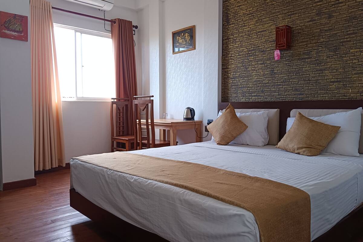Une chambre d’hôtel avec un grand lit, des chaises en bois, une petite table et un climatiseur fixé au mur.