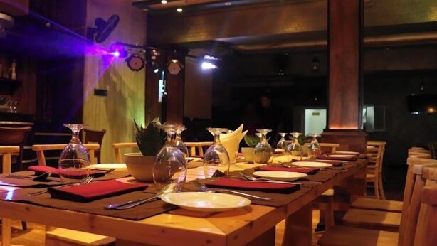 A restaurant with wooden tables and chairs, a long counter, and a bar area. - La Cozy Hotel & Restaurant (Negombo)