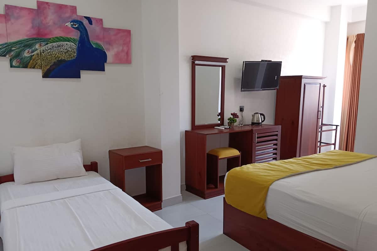 Une chambre d’hôtel avec deux lits, un bureau en bois, une télévision et un tableau représentant un paon accroché au mur.