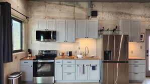 A modern kitchen with stainless steel appliances, grey cabinets, and a concrete wall. - Cigar Mountain House (Brewster County)