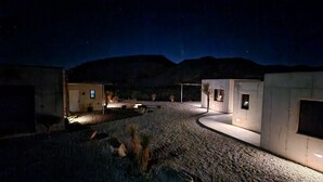 A desert-style building with multiple rooms, a gravel driveway, and a mountainous backdrop. - Cigar Mountain House (Brewster County)
