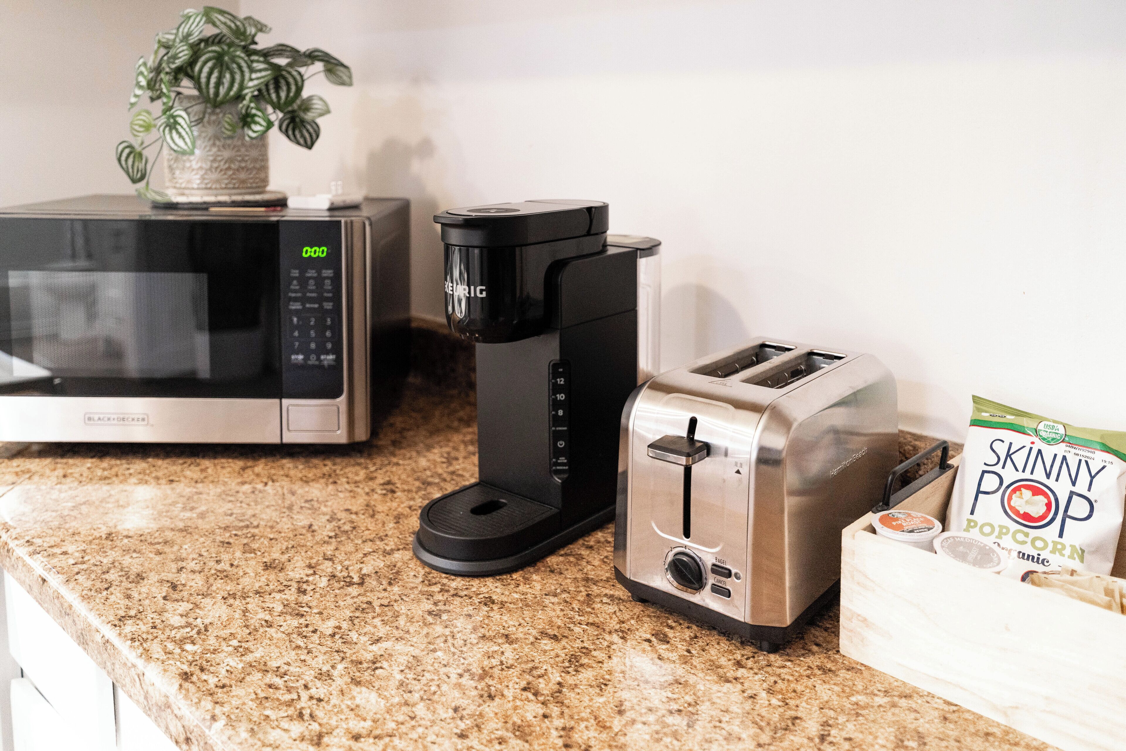 Una encimera de cocina con microondas, cafetera, tostadora y una bolsa de palomitas Skinny Pop.