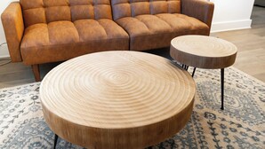 Un divano in pelle marrone e due tavolini rotondi in legno con un motivo circolare sul piano.