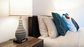 Una camera da letto ordinata con comodino, lampada e un letto con molti cuscini.