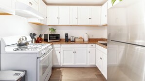 Una cucina moderna con mobili bianchi, un frigorifero in acciaio inossidabile, un forno a microonde, un fornello e una macchina da caffè.