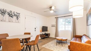 Un soggiorno moderno con un tavolo da pranzo rotondo, sedie arancioni, un divano, una TV e una ventola a soffitto.