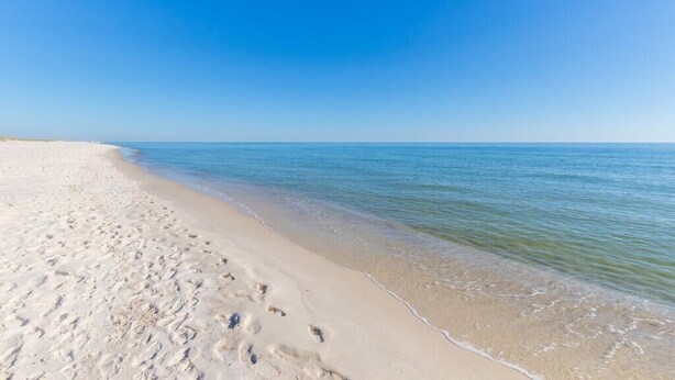 A beach with footprints leading to the water, clear skies, and calm sea.