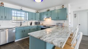 A modern kitchen with teal cabinets, a marble countertop, stainless steel appliances, and a central island.