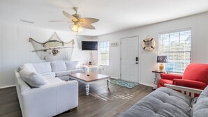 A living room with a white sofa, a red chair, a wooden coffee table, a ceiling fan, and a television mounted on the wall.