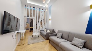 Ett modernt vardagsrum med en grå soffa, en tv och ett trägolv.