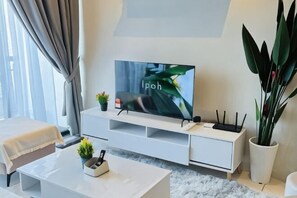A modern living room with a flat-screen TV, white furniture, a potted plant, and a window with curtains. - The Horizon Ipoh By Iconique Espace (Ipoh)