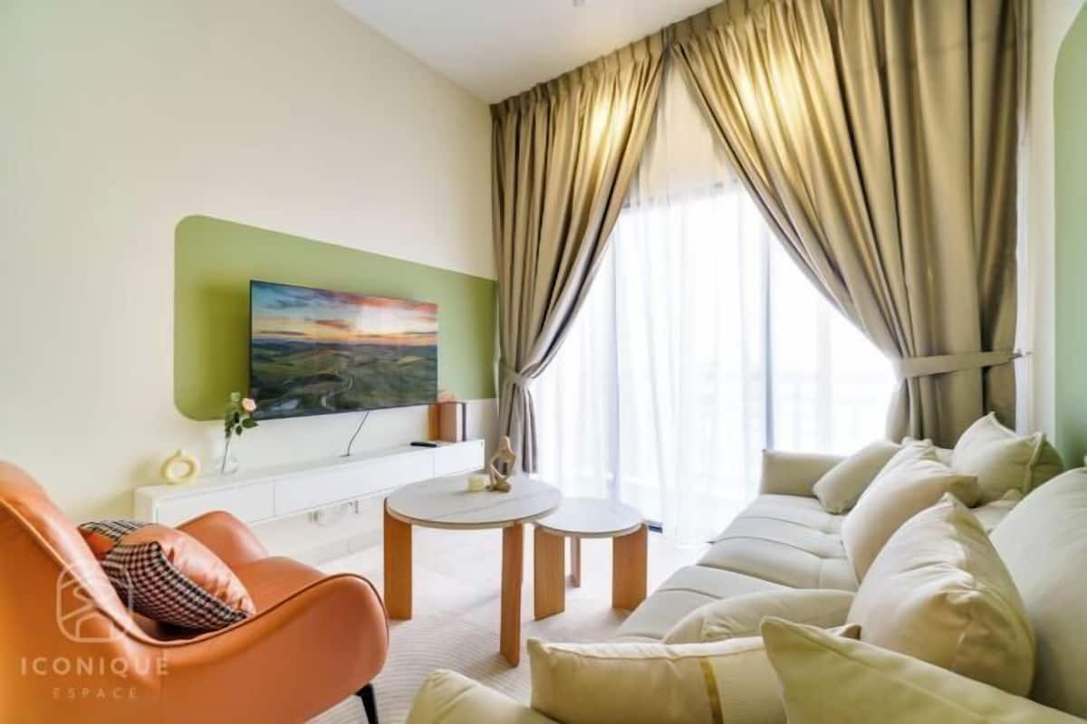 A modern living room with a sofa, a coffee table, and a flat-screen TV mounted on a green accent wall.
