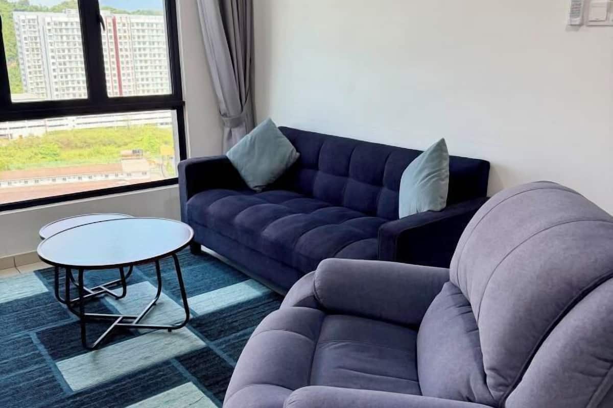 A living room with a sofa, a round table, and a view of buildings through a window.