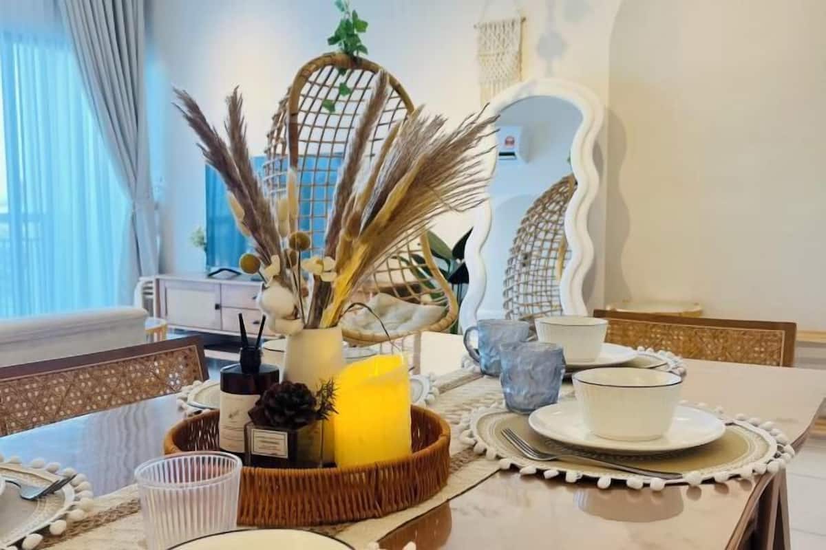 A dining table with a candle, a vase with dried plants, and a woven basket.