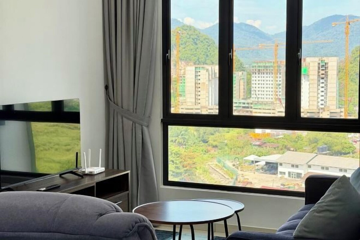 A modern hotel room with a large window offering a view of a cityscape and mountains.