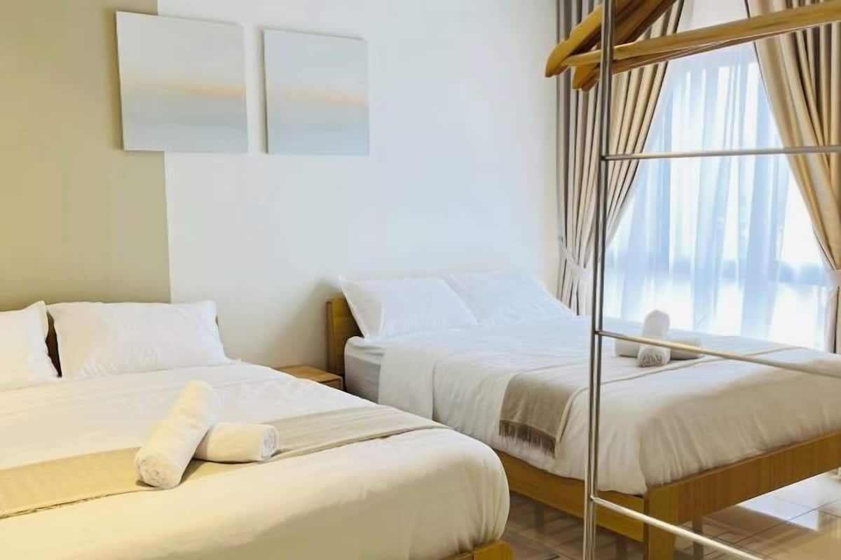 A hotel room with two beds, a large window with curtains, and a wall-mounted artwork.