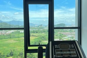 A room with a large window offering a view of a green landscape and distant buildings. - The Horizon Ipoh By Iconique Espace (Ipoh)