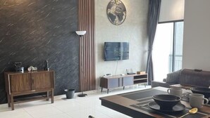 A modern living room with a dining area, a wooden cabinet, a TV mounted on the wall, and a large window with curtains.