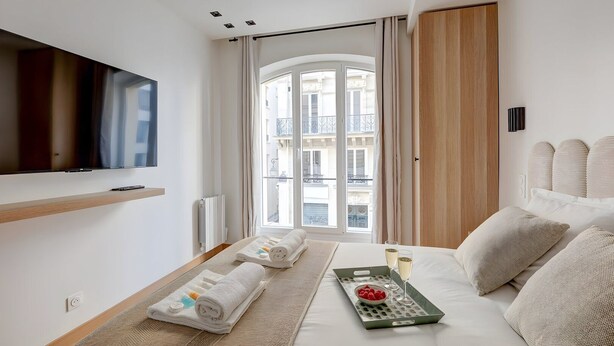 Ein modernes Hotelzimmer mit großem Fenster, Flachbildfernseher, Bett mit Frühstücksbrett und Blick auf die Stadt.