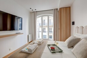 Ein modernes Hotelzimmer mit großem Fenster, Flachbildfernseher, Bett mit Frühstücksbrett und Blick auf die Stadt.