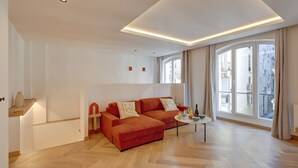 Ein modernes Wohnzimmer mit einem roten Sofa, einem kleinen Tisch mit Getränken und großen Fenstern mit Blick auf die Stadt.