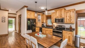 A modern kitchen with wooden cabinets, stainless steel appliances, and a dining area with a wooden table and chairs. - The Enclave at Cumberland (Albany)