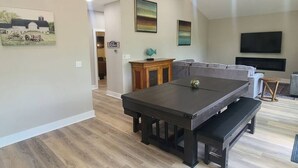 A living room with a dark wooden table, a gray sofa, and a flat-screen TV mounted on the wall. - The Enclave at Cumberland (Albany)
