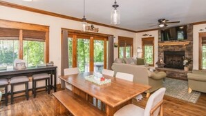 A spacious living room with a wooden dining table, a fireplace, and a large window offering a view of the outdoors. - The Enclave at Cumberland (Albany)