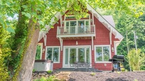 A two-story red house with a balcony, surrounded by greenery. - The Enclave at Cumberland (Albany)